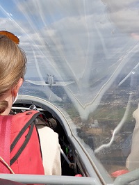 Blick aus dem Segelflug-Cockpit beim F-Schlepp Foto aus dem Cockpit eines Segelflugzeugs im Schlepp-Flug. Links ist die Pilotin von hinten zu sehen, rechts vorne sieht man das schleppende Motorflugzeug, eine DR 401.